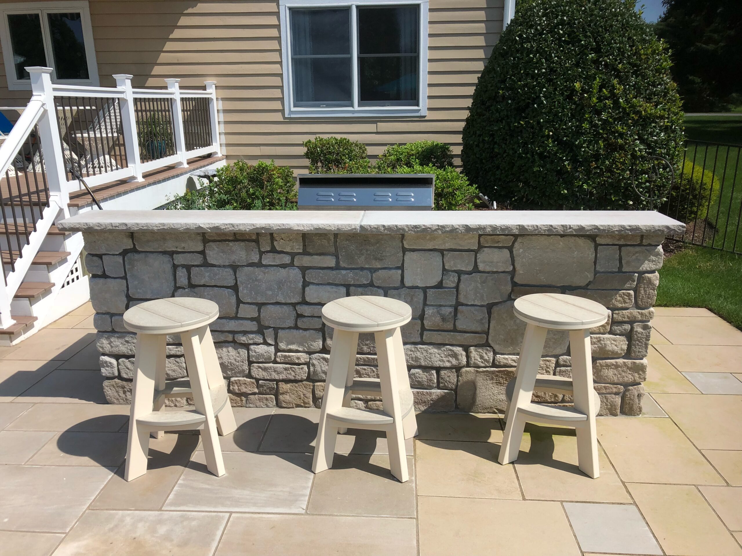 Stone outdoor bar with four stools on a paver patio