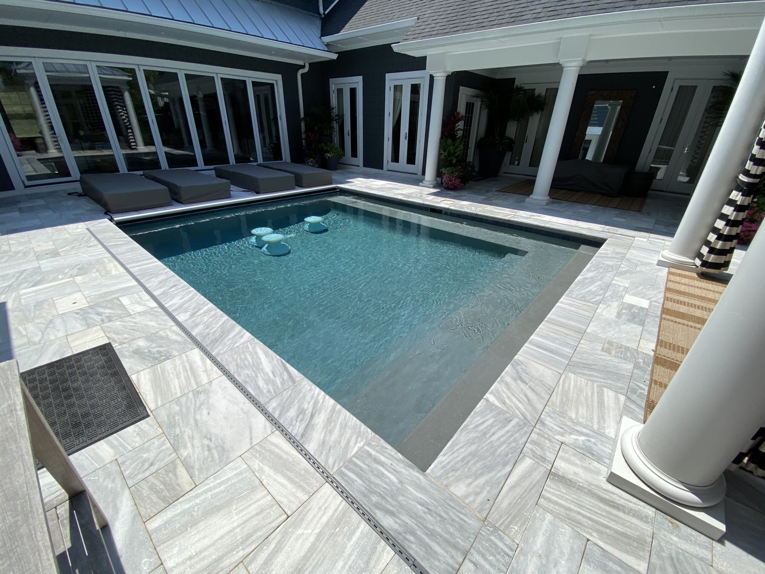 Pool surrounded by a paved terrace beside a home