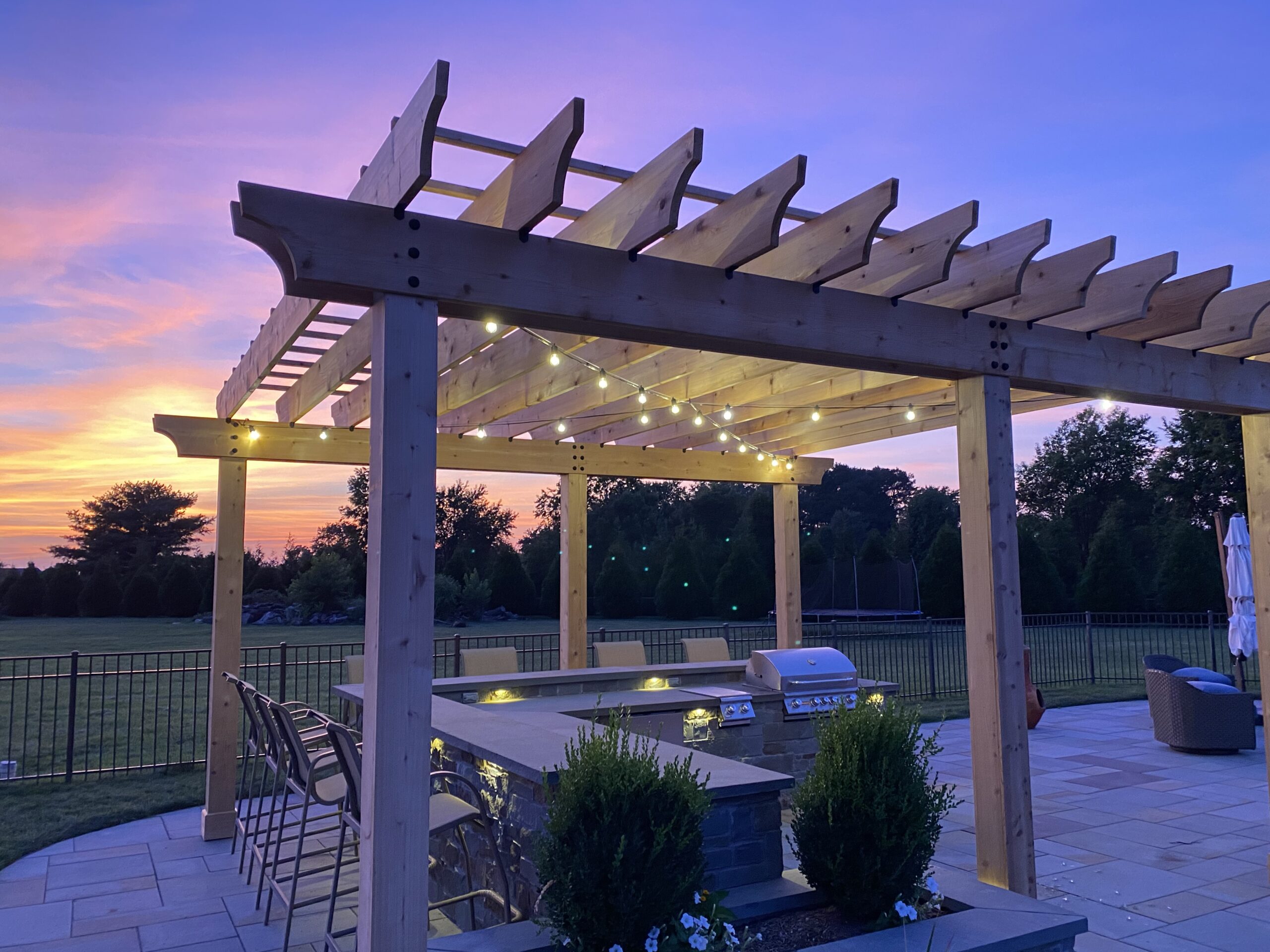 Outdoor kitchen beneath a pergola with string lights at sunset