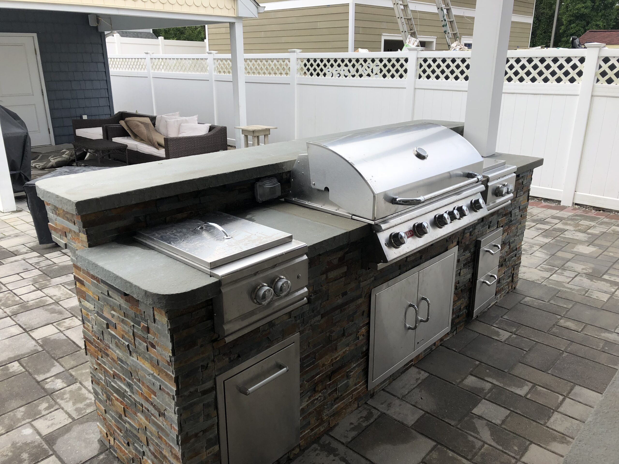 Built-in stainless steel grill and side burner in a stacked-stone outdoor kitchen