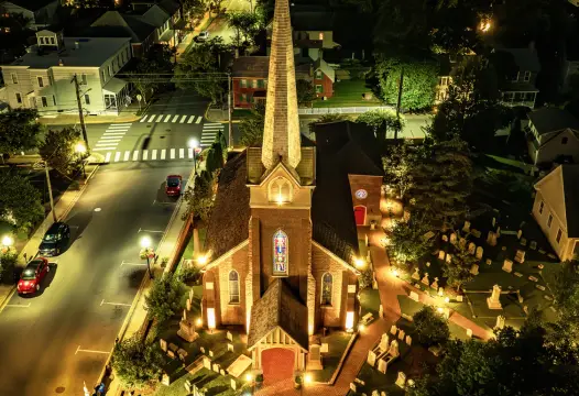 Aerial nighttime view of an illuminated property with buildings, paths, and trees