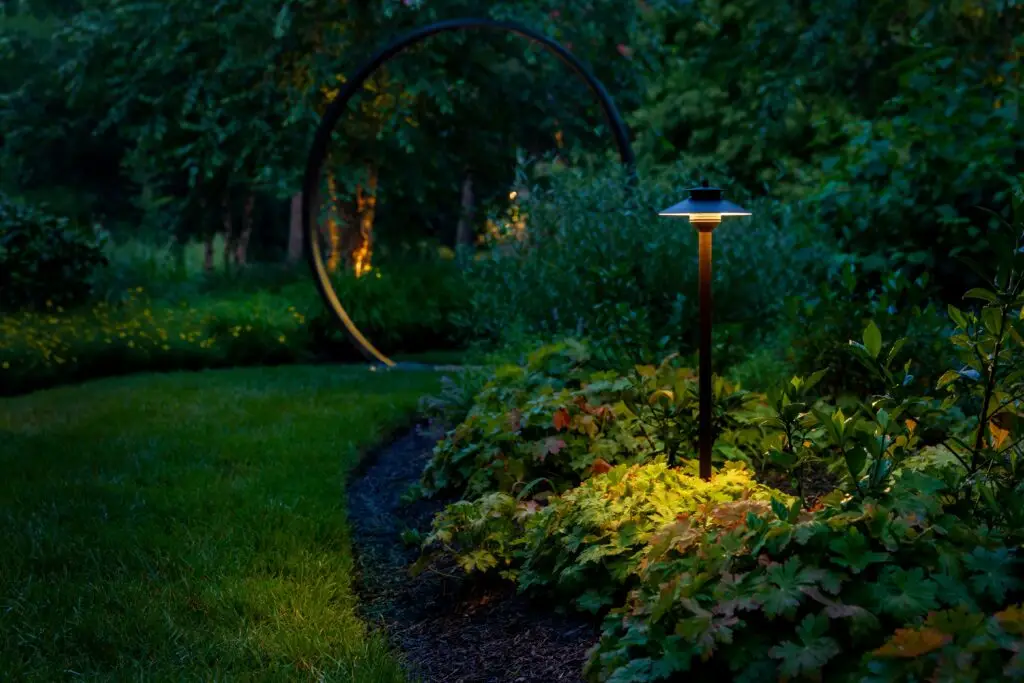 Path light illuminating garden planting beside a lawn