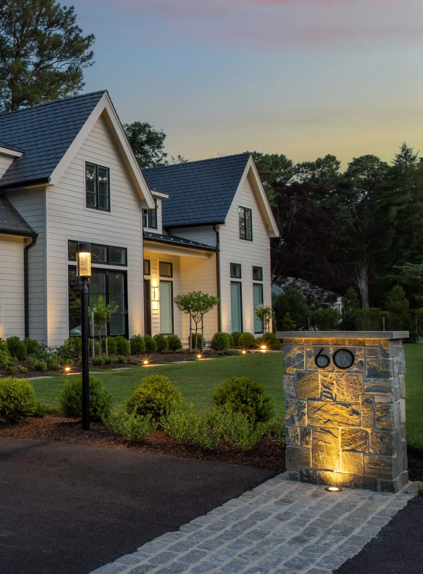 An illuminated stone entry feature, landscape planting, and a path at a Bella Terra residential project