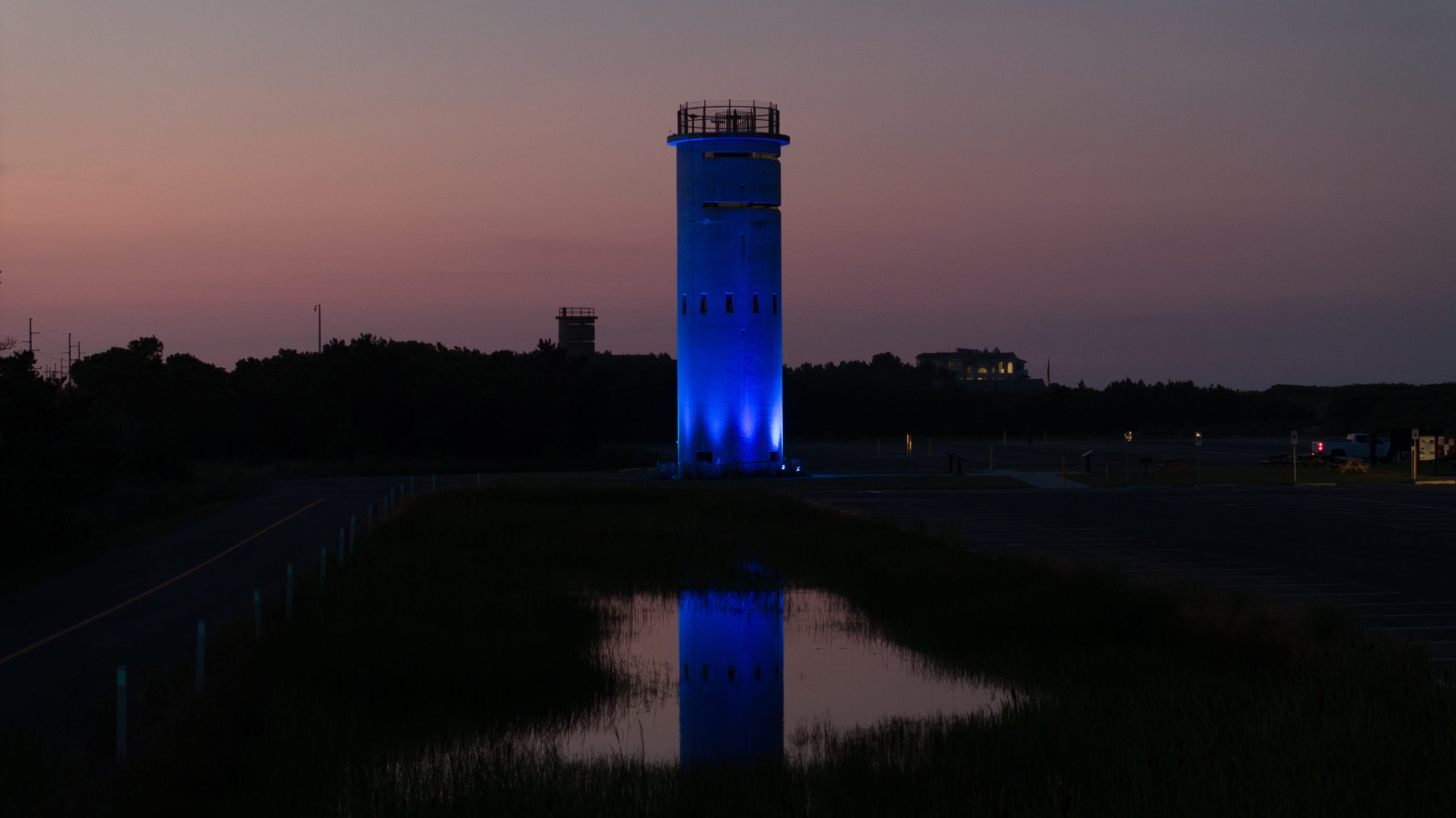 Blue architectural lighting illuminating a coastal observation tower at sunset
